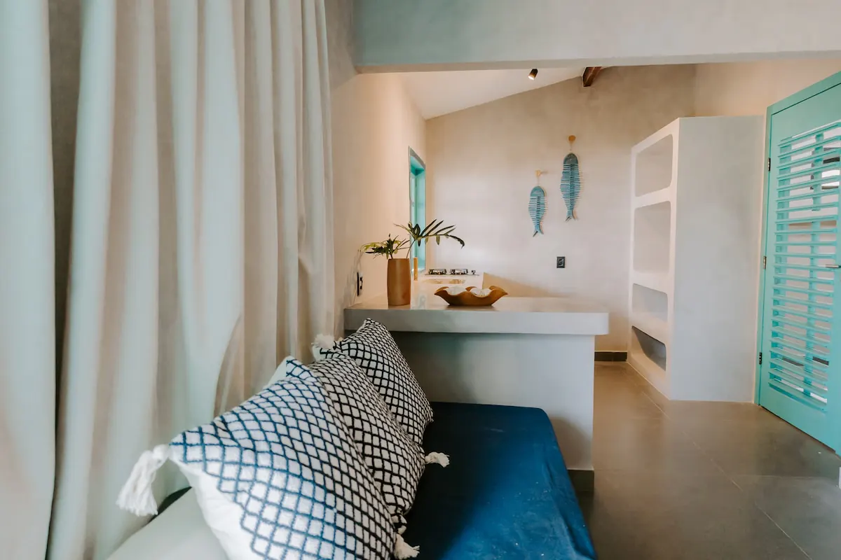 Sala da suíte com sofá azul, bancada e porta de veneziana verde-água